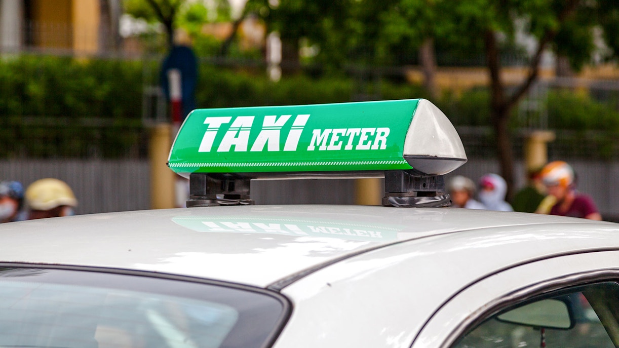 Vietnamese taxi with green taxi meter sign on roof.