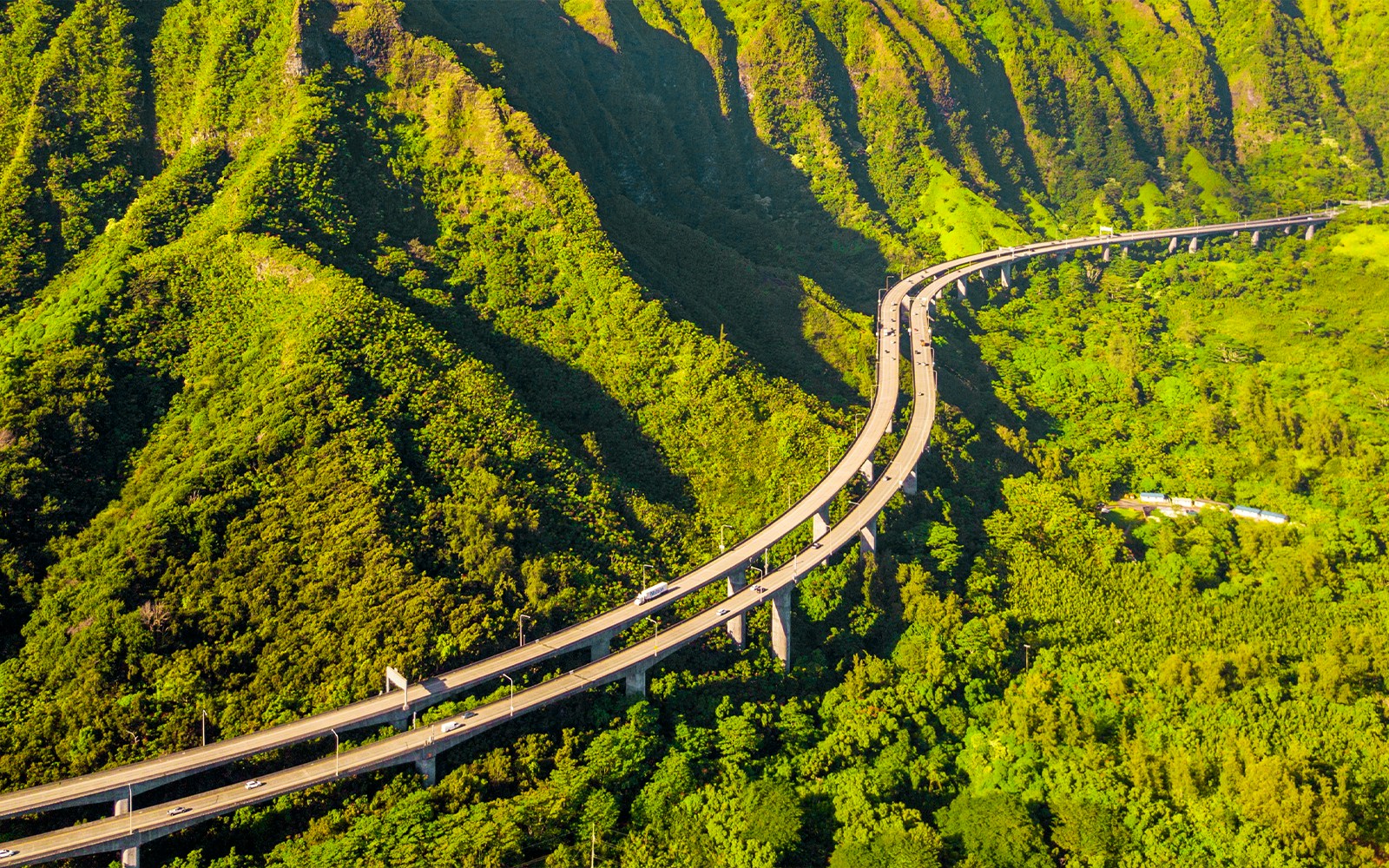 Aerial view of lush green mountains and winding road at Kualoa Ranch, Oahu, Hawaii.