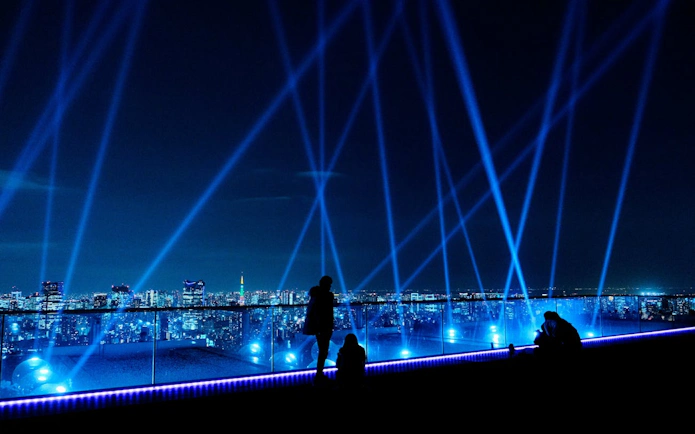 Tokyo skyline view from Shibuya Sky at night with blue lights and cityscape.