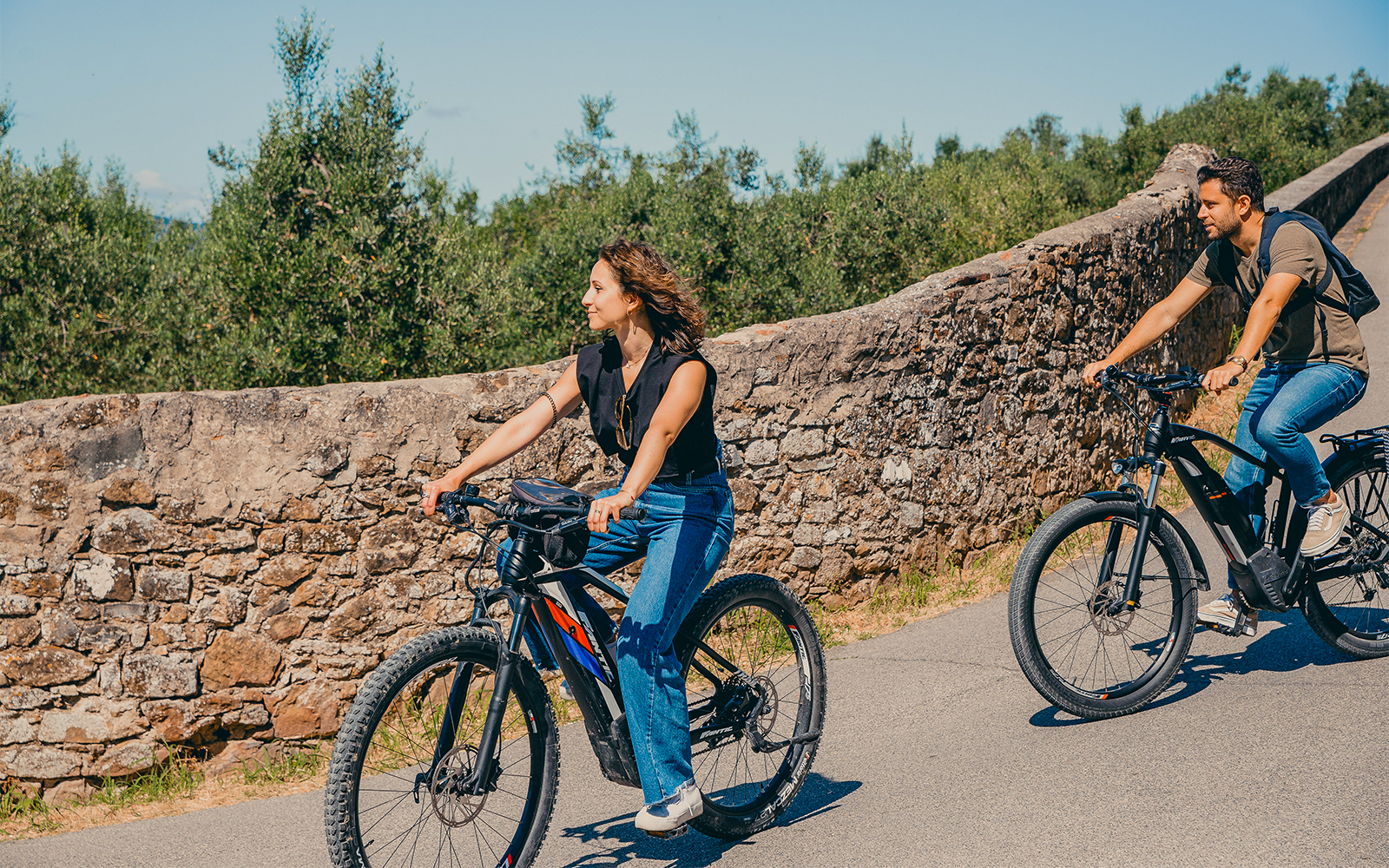 Cyclists on electric bikes ride along a stone wall in the hills of Florence.