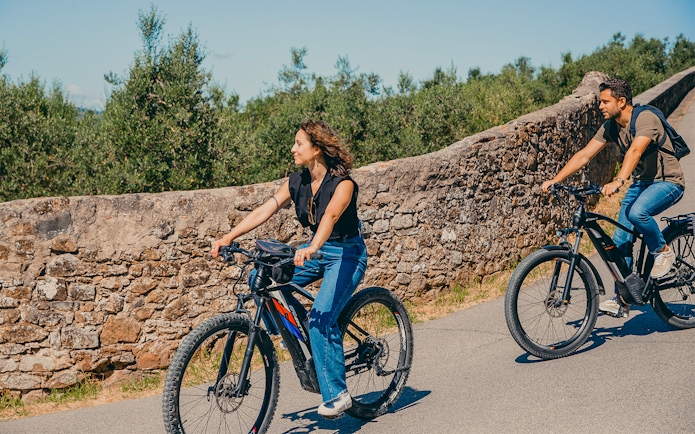 Cyclists on electric bikes ride along a stone wall in the hills of Florence.