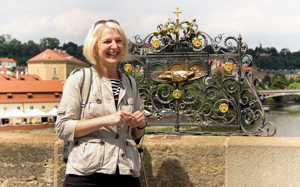 Smiling tourist at Charles Bridge, Prague, with decorative railing and river view.