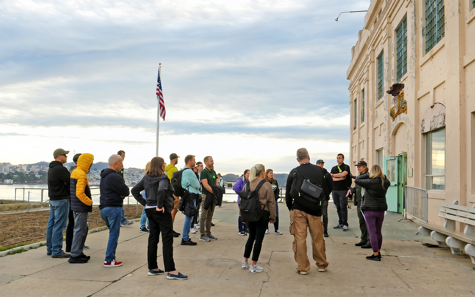Group on guided tour outside Alcatraz Island building, San Francisco Bay in background.