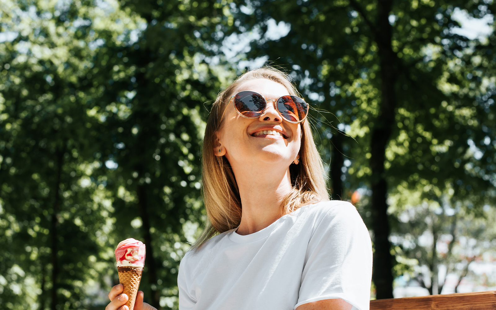 Woman wearing sunglasses holding ice cream in a sunny park.