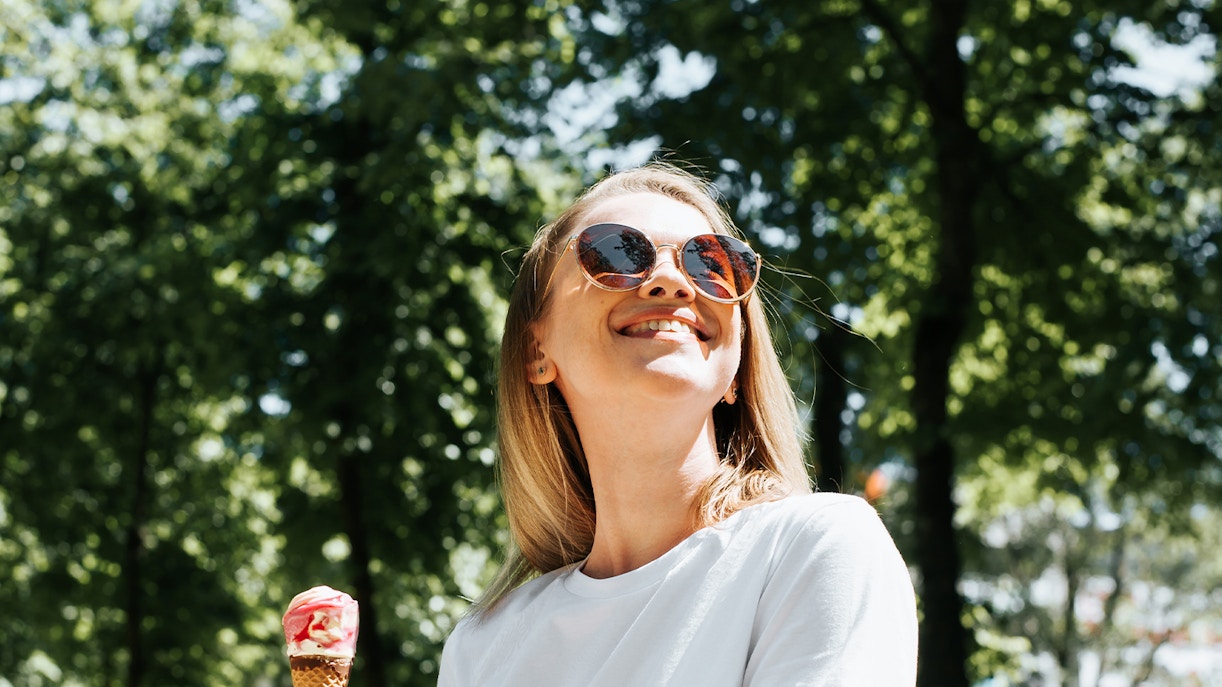 Woman wearing sunglasses holding ice cream in a sunny park.