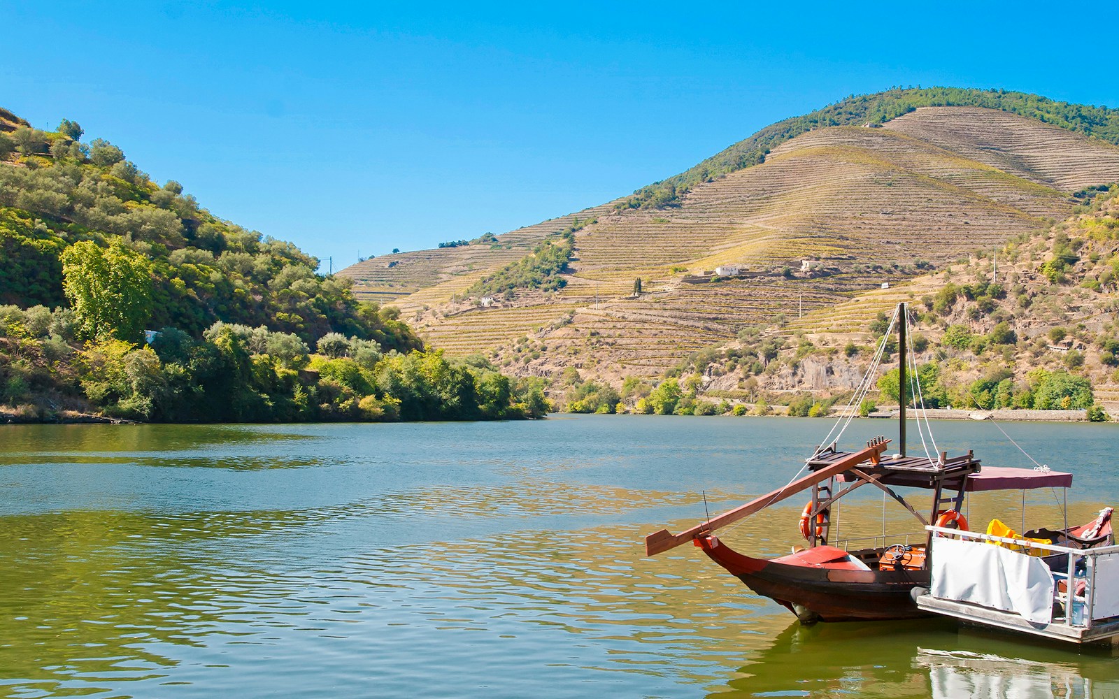 Traditional boat on Douro River near Pinhão Pier with terraced vineyards in the background.