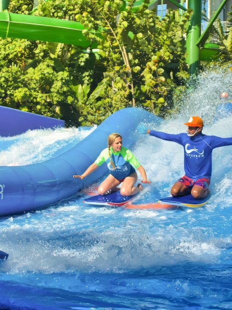 Instructor guiding a girl on a surfboard at Flow Rider, Waterbom Bali water park.
