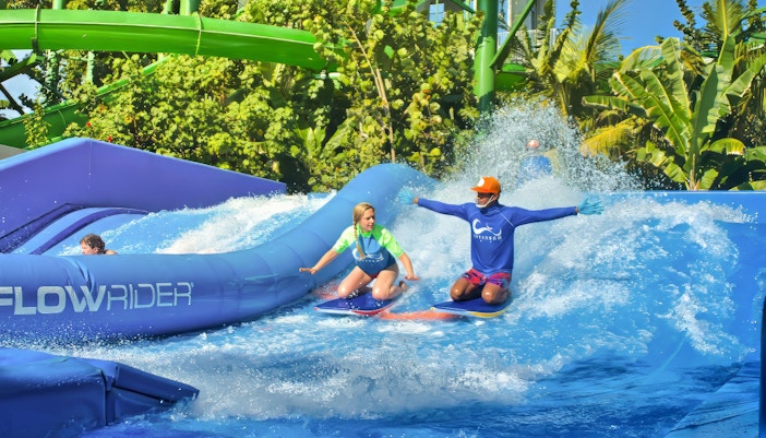 A boy surfing at the Flow Rider at Waterbom Bali water park with the help of a guide.