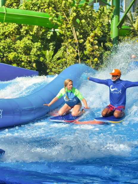 Instructor guiding a girl on a surfboard at Flow Rider, Waterbom Bali water park.