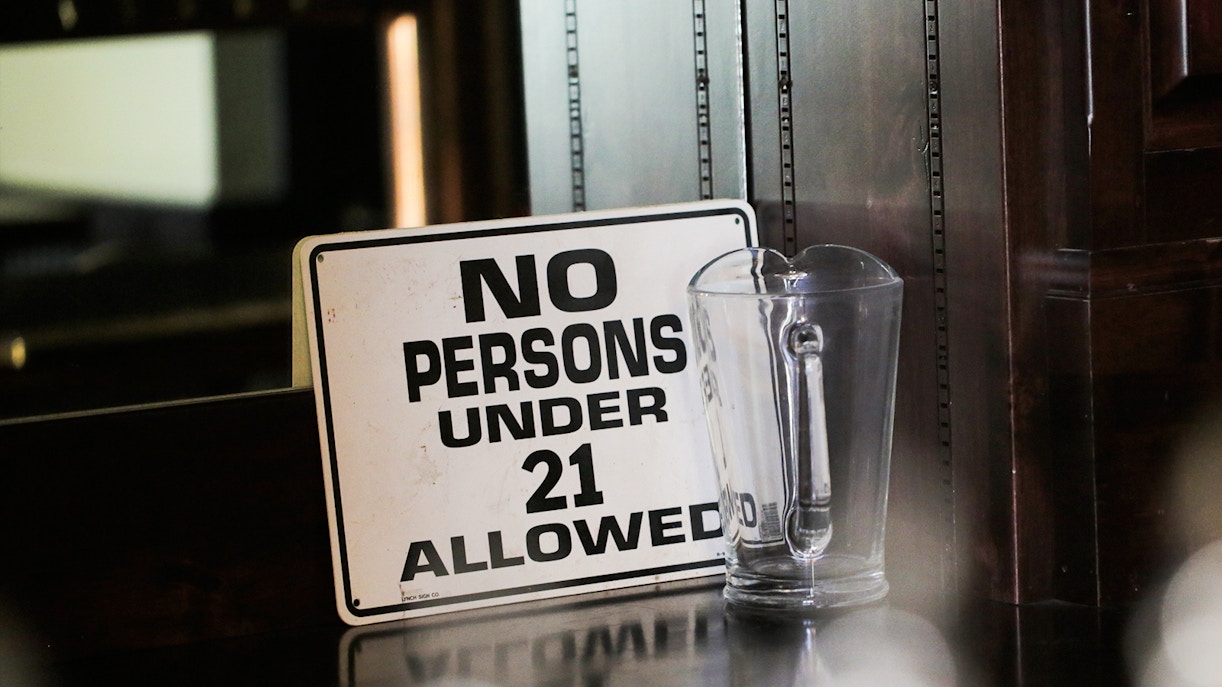 No persons under 21 allowed sign next to a glass pitcher on a bar counter.