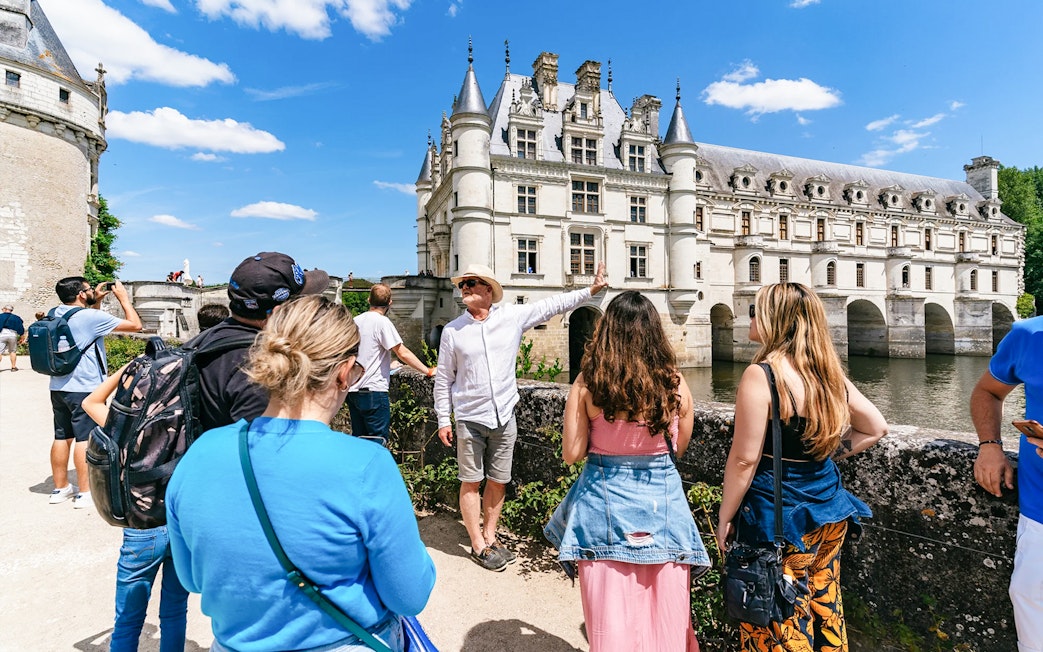 Tour group at Chenonceau Castle with guide pointing at the historic architecture.