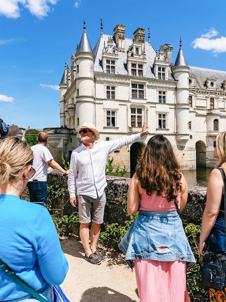 Tour group at Chenonceau Castle with guide pointing at the historic architecture.