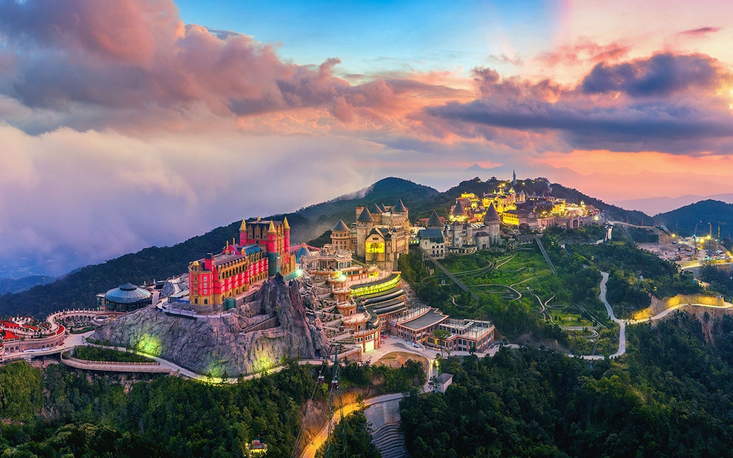 Sunset view of Sun World Ba Na Hills with illuminated castles and lush landscape in Da Nang, Vietnam.