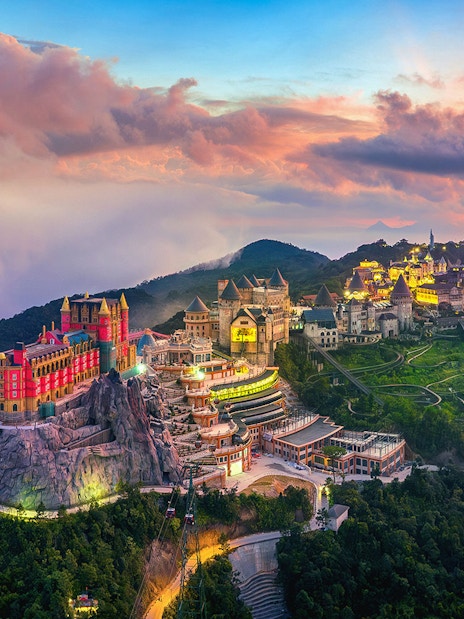 Sunset view of Sun World Ba Na Hills with illuminated castles and lush landscape in Da Nang, Vietnam.