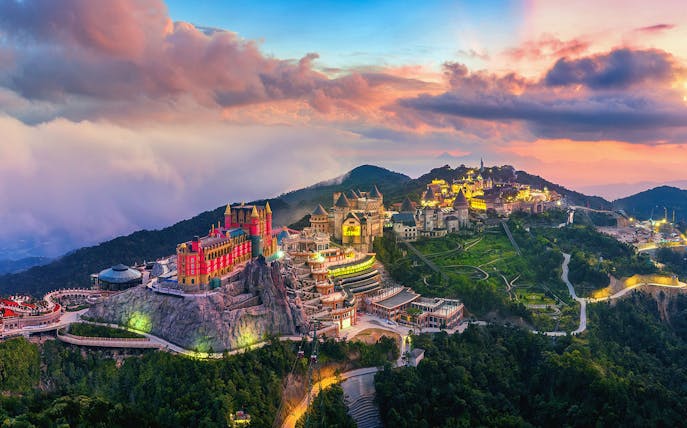 Sunset view of Sun World Ba Na Hills with illuminated castles and lush landscape in Da Nang, Vietnam.
