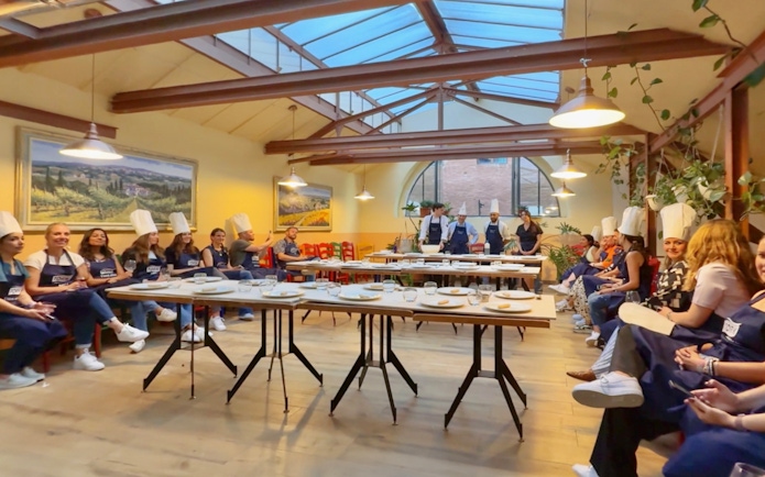 Participants in chef hats listening during a cooking class briefing in Siena.