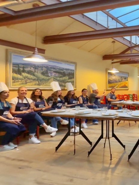 Participants in chef hats listening during a cooking class briefing in Siena.