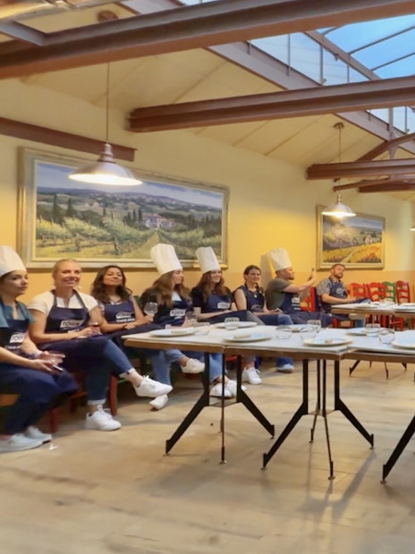 Participants in chef hats listening during a cooking class briefing in Siena.