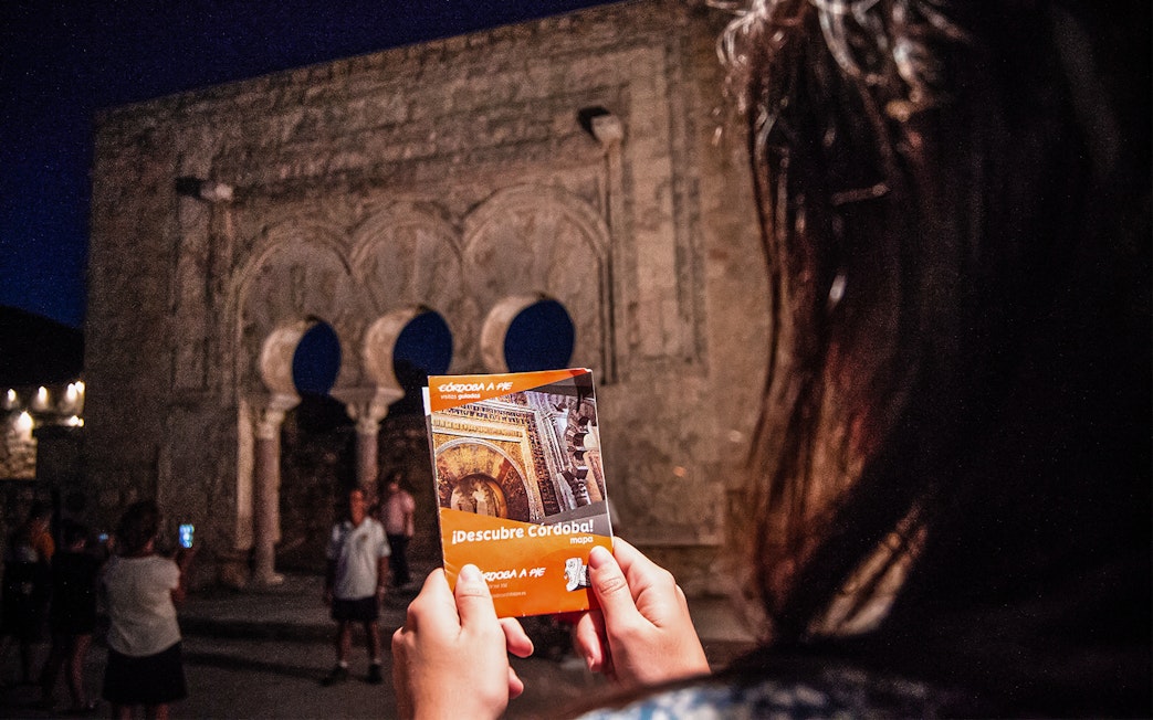 Guided night tour at Medina Azahara with visitors holding a Córdoba map.