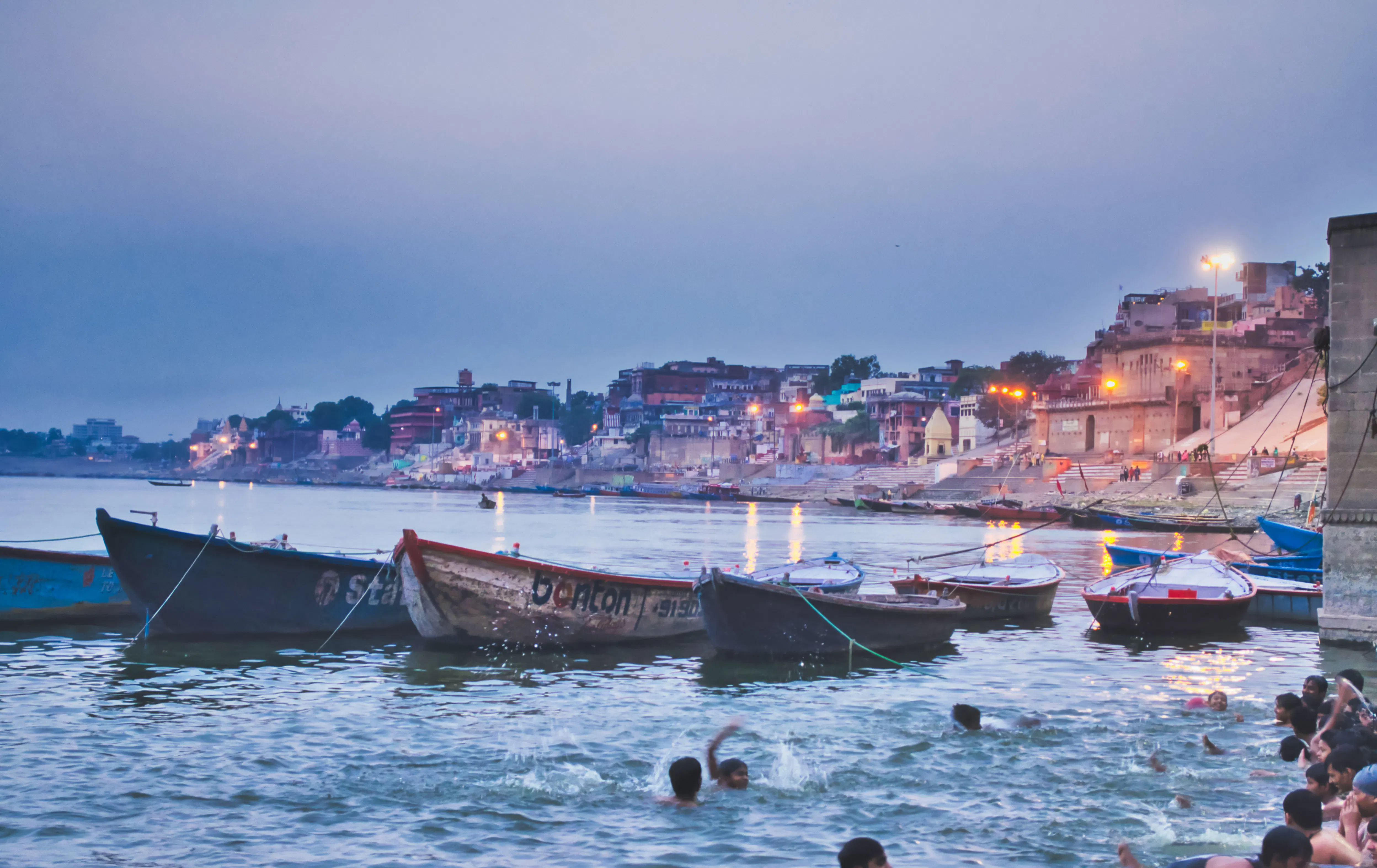 Boats on the Ganges River at sunrise with Varanasi ghats in the background.