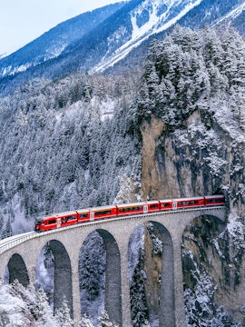 Bernina Express crossing a snowy viaduct in the Swiss Alps.
