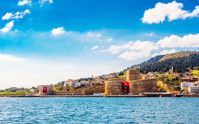 Gallipoli Peninsula fortress with Turkish flags, viewed from the water, on a sunny day.