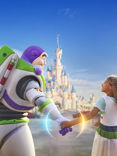 Buzz Lightyear holding hands with a child in front of Sleeping Beauty Castle at Disneyland Paris.
