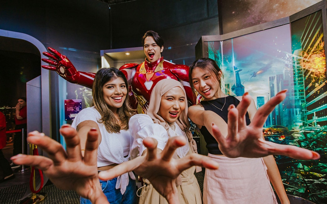 Three people posing with Iron Man wax figure at Madame Tussauds Singapore.