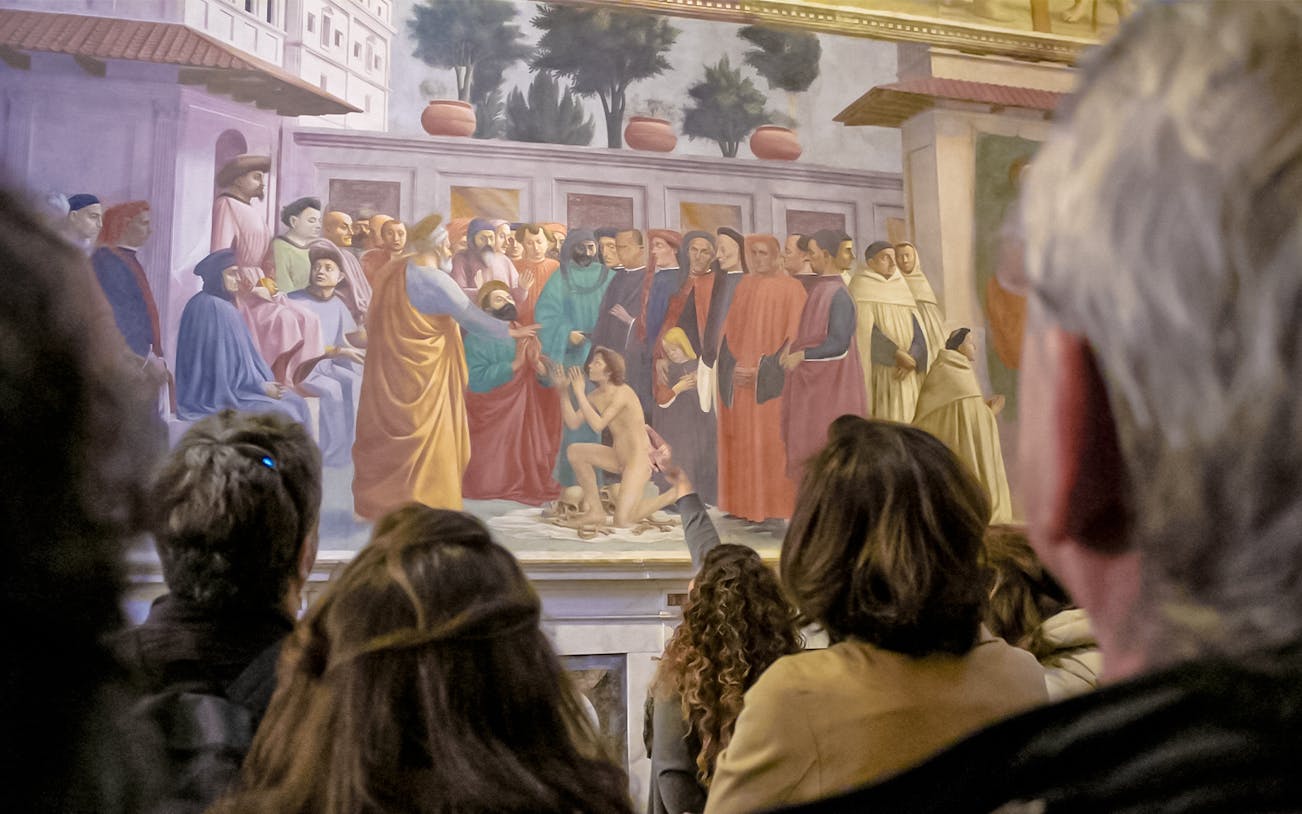 Guide with visitors observing frescoes at Brancacci Chapel, Florence, Italy.