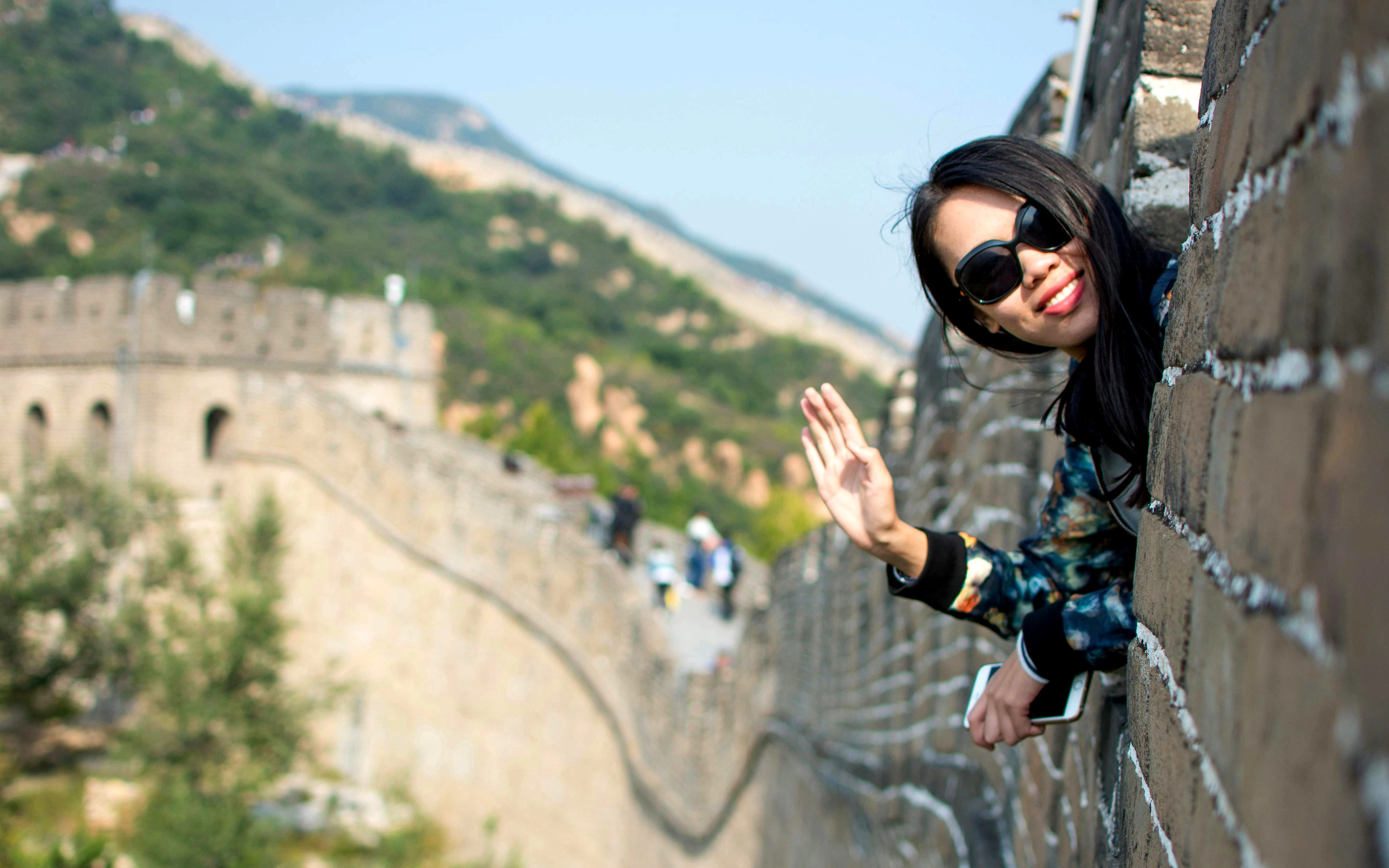 Tourist waving on the Great Wall of China with scenic view.