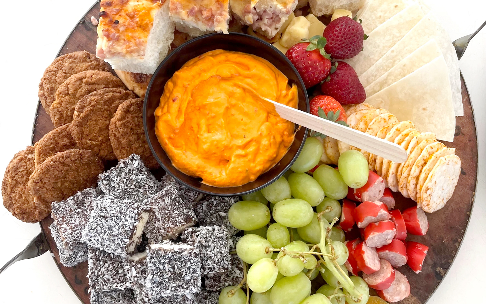 Aussie bites platter with lamingtons, crackers, dip, grapes, and strawberries on Sydney Harbour catamaran cruise.