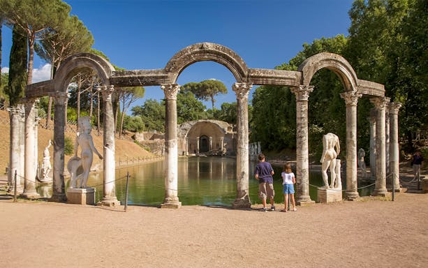 Statues and columns at the Canopus in Hadrian's Villa, Tivoli, with visitors observing.
