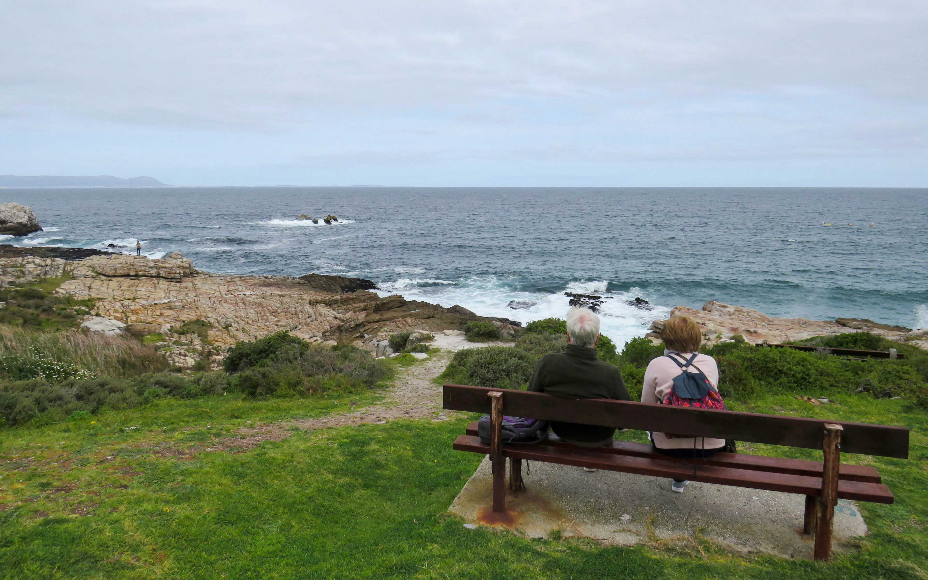Couple sitting on a bench overlooking the ocean in Hermanus, South Africa.