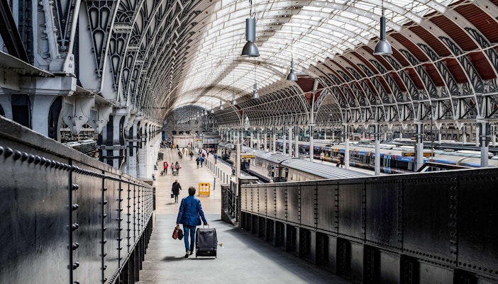 Traveler with luggage walking through London Paddington Station concourse.
