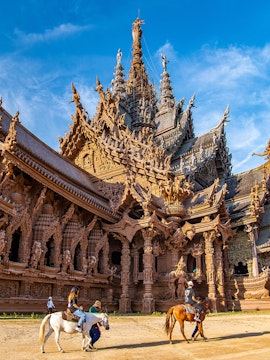 Visitors on horseback in front of the intricate wooden Sanctuary of Truth in Pattaya, Thailand.
