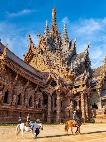 Visitors on horseback in front of the intricate wooden Sanctuary of Truth in Pattaya, Thailand.