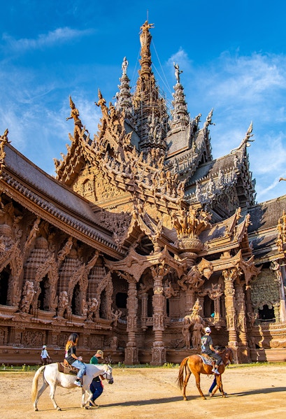 Visitors on horseback in front of the intricate wooden Sanctuary of Truth in Pattaya, Thailand.
