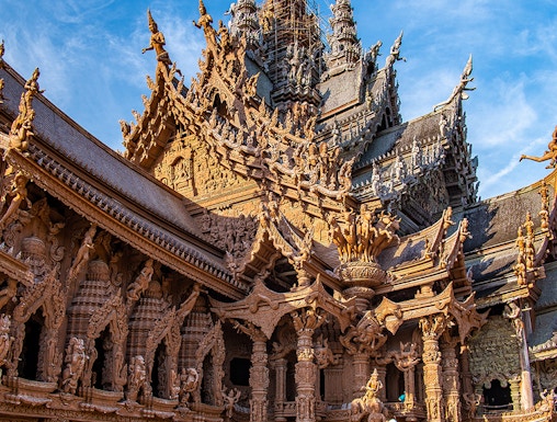 Visitors on horseback in front of the intricate wooden Sanctuary of Truth in Pattaya, Thailand.