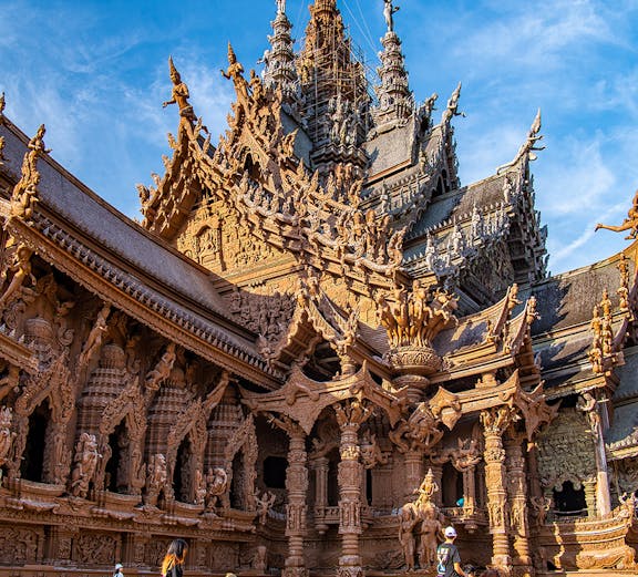 Visitors on horseback in front of the intricate wooden Sanctuary of Truth in Pattaya, Thailand.
