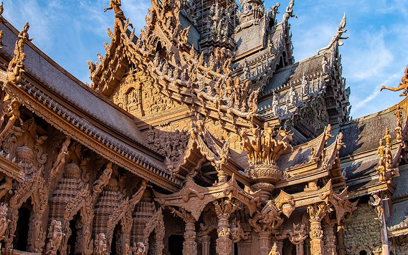 Visitors on horseback in front of the intricate wooden Sanctuary of Truth in Pattaya, Thailand.