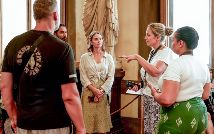 Tour guide explaining artwork to visitors inside Uffizi Gallery, Florence.