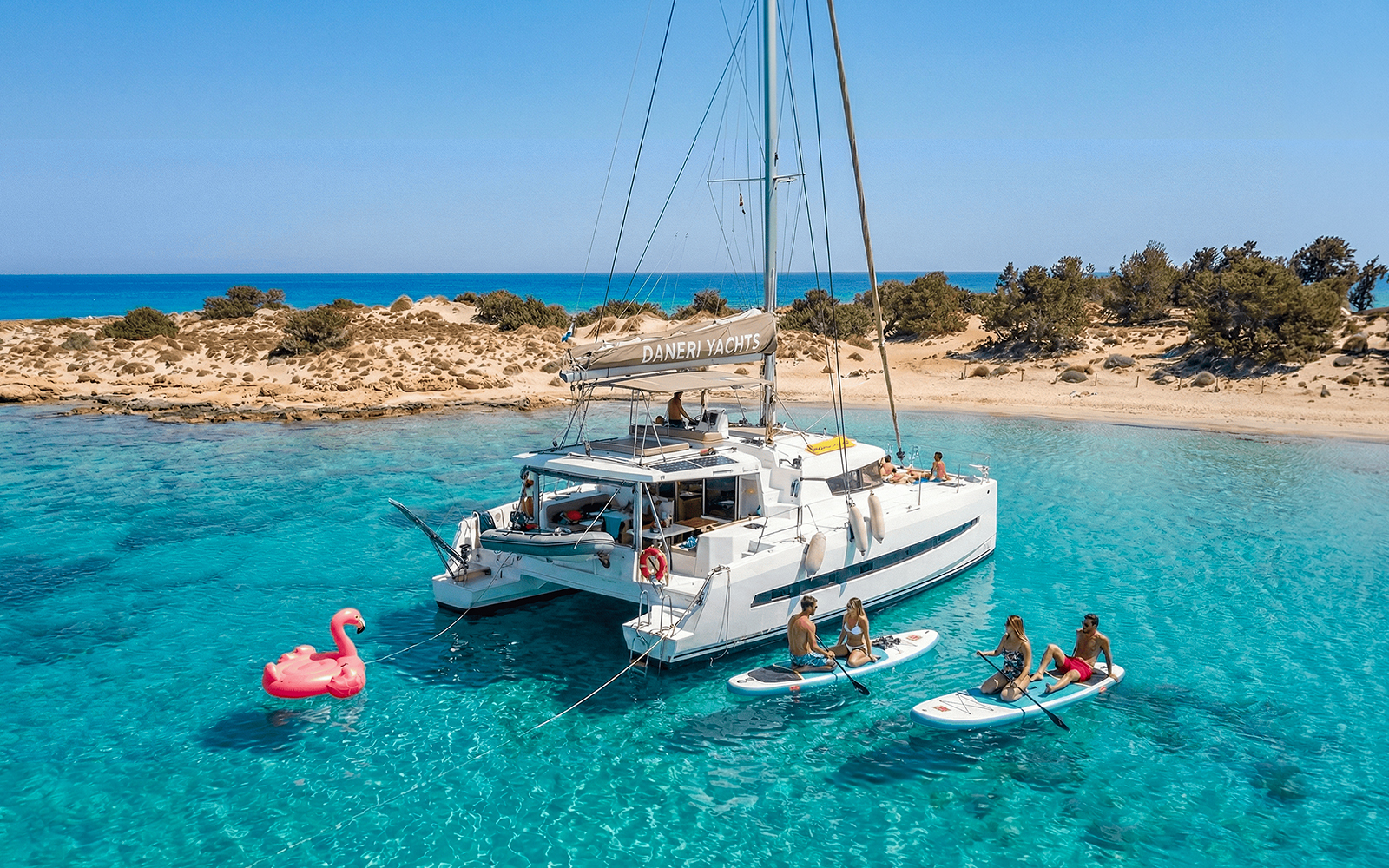 Catamaran anchored near Chrissi Island with people paddleboarding in clear waters.