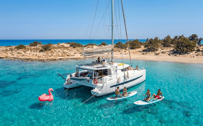 Catamaran anchored near Chrissi Island with people paddleboarding in clear waters.