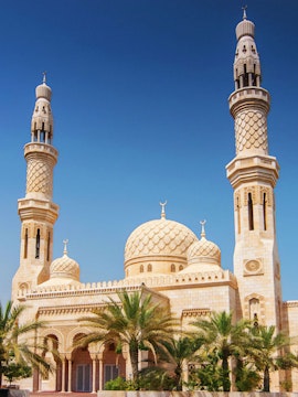 Jumeirah Mosque in Dubai with palm trees under a clear blue sky.