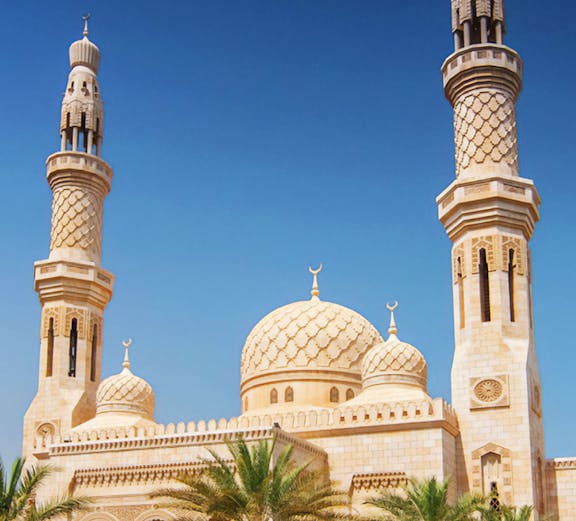 Jumeirah Mosque in Dubai with palm trees under a clear blue sky.