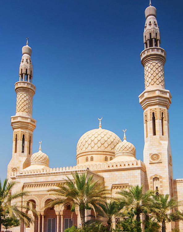 Jumeirah Mosque in Dubai with palm trees under a clear blue sky.