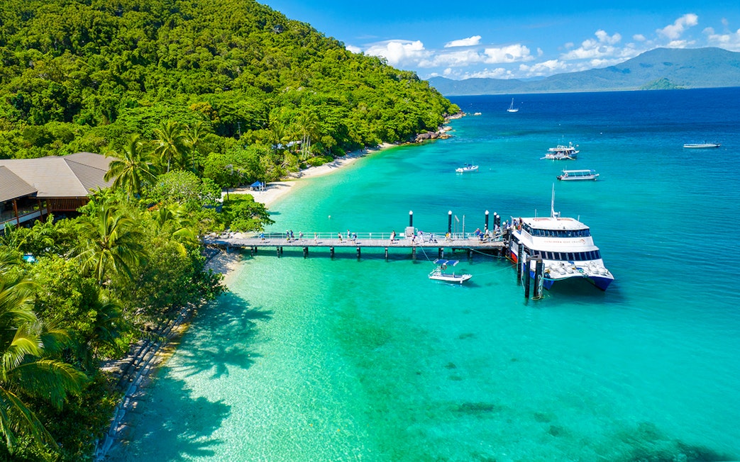 Fitzroy Island pier with tour boat, clear waters, and lush greenery, Cairns day trip.