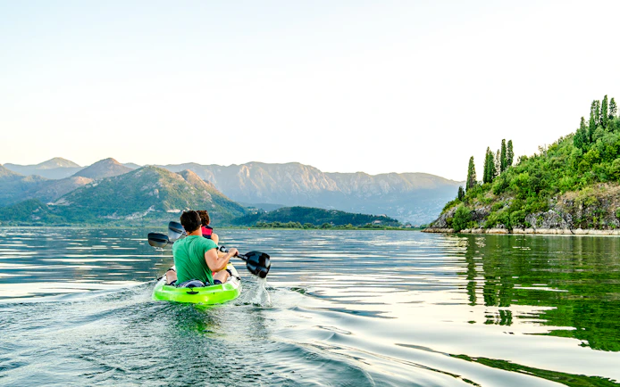Kayakers paddling on Lake Skadar with mountainous landscape in Montenegro.