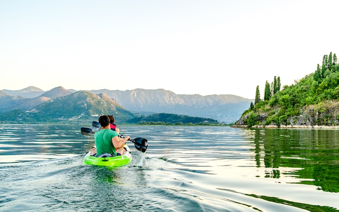 Kayakers paddling on Lake Skadar with mountainous landscape in Montenegro.