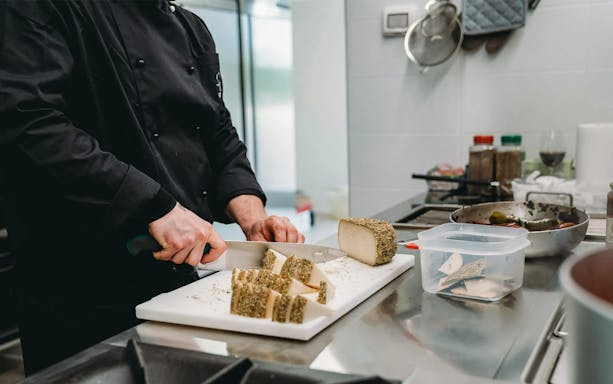 Chef slicing cheese during Tuscan cooking class with lunch preparation.